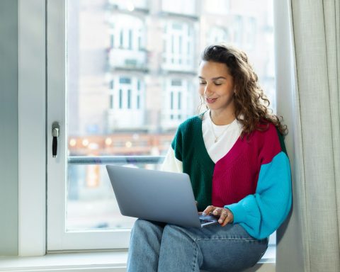 a woman sitting on a window sill using a laptop