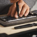 Een smartphone die wordt opengebroken voor reparatie, met schroeven en gereedschap op tafel