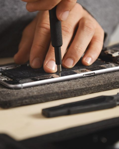 Een smartphone die wordt opengebroken voor reparatie, met schroeven en gereedschap op tafel