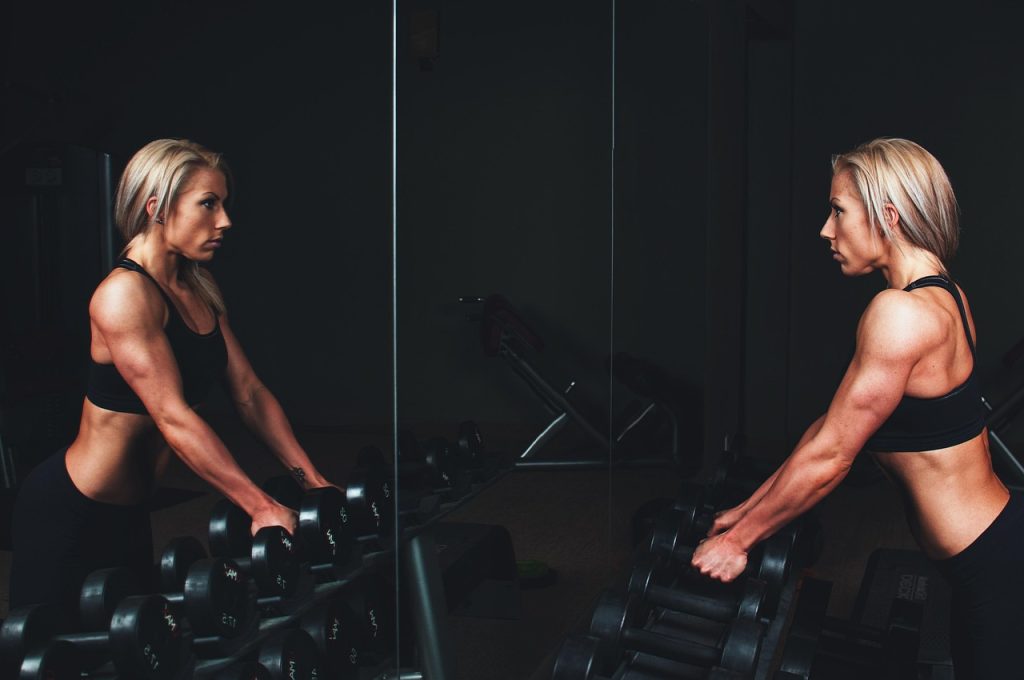 Persoon op een crosstrainer in de sportschool met een smartphone waarop een fitness-app open staat