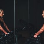 Persoon op een crosstrainer in de sportschool met een smartphone waarop een fitness-app open staat