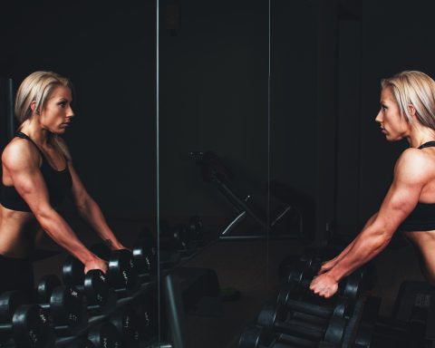 Persoon op een crosstrainer in de sportschool met een smartphone waarop een fitness-app open staat