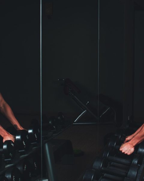 Persoon op een crosstrainer in de sportschool met een smartphone waarop een fitness-app open staat