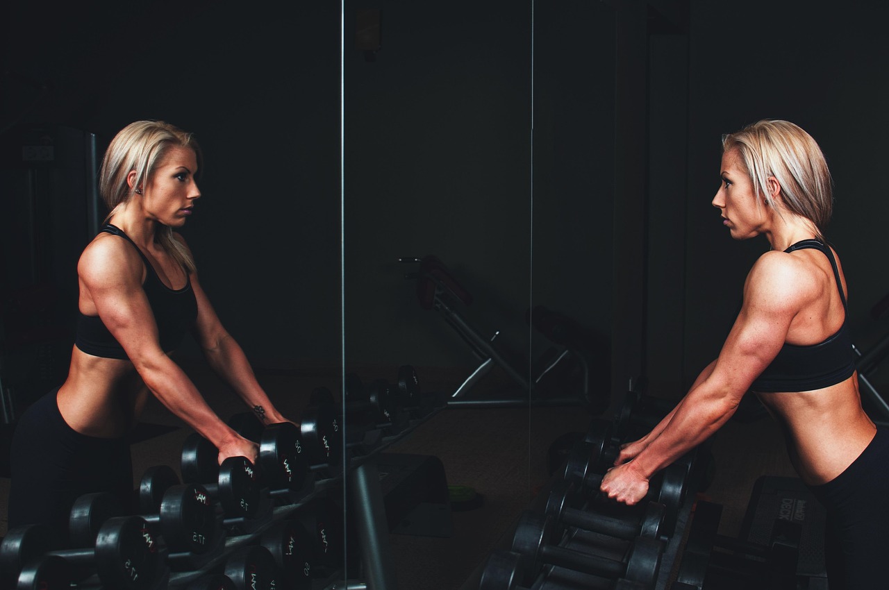 Persoon op een crosstrainer in de sportschool met een smartphone waarop een fitness-app open staat